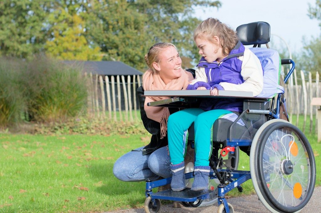 mother kneeling beside her daughter in wheelchair with disability
