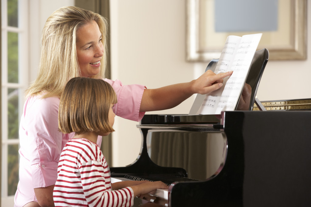 mother teaching her daughter how to play piano