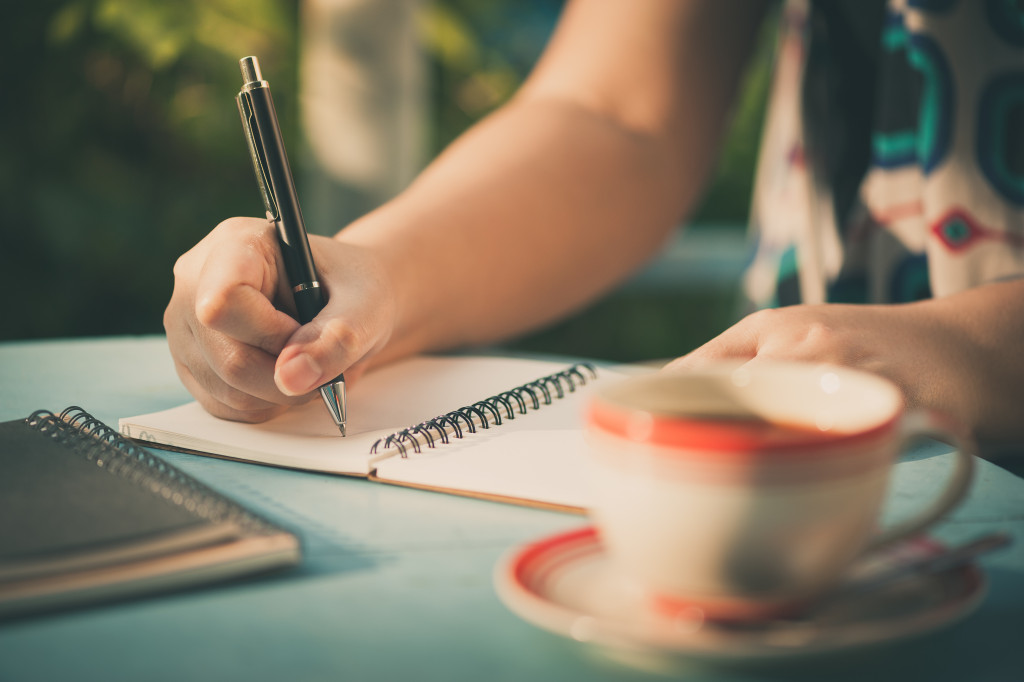 Woman hand writing journal on small notebook at outdoor area in cafe with morning